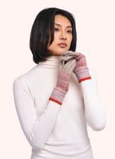 A woman in a white turtleneck, wearing a pair of gloves with a geometric orange, purple and gold pattern on them against a light background.