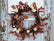 Grapevine wreath decorated with beech leaves, white wood flowers, bunny tail, and buttons. The wreath hangs against a grey wooden door. 
