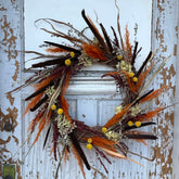 Grapevine wreath decorated with dried hydrangeas, cattails, yellow crespedia, and other dried and fall elements. The wreath hangs on a grey wooden door.