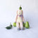 Hand-knit pink and cream bunny, sitting with veggies and leaves around it against a white background.