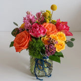 A petit floral arrangement in a bright color palette, placed in a clear mason-jar style vase with a hobnail design.