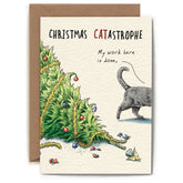 Greeting card with an illustration of the top part of a Christmas tree laying on the ground with bulbs and garland laying around it. The back half of a grey cat walks off on the right side, and the card reads "Christmas Catastrophe", with a speech bubble above the cat that says "my work here is done".