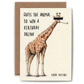 A greeting card with a brown envelope behind it. The card features an illustration of a giraffe with a black bar covering its eyes, with the text 'GUESS THE ANIMAL TO WIN A BIRTHDAY DRINK' and 'YOURE BUYING!' on an off-white background.