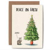 Greeting card with an illustration of a grey and white cat standing next to a Christmas tree that's decorated on the top third, out of the cat's reach. The card reads "Peace on Earth", and the cat has a speech bubble above its head that says "Damn".