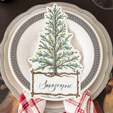 A table setting with white plates with brown and gold trim. A place setting with an illustration of a cedar tree sits atop the plates.