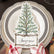A table setting with white plates with brown and gold trim. A place setting with an illustration of a cedar tree sits atop the plates.