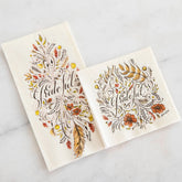 A guest napkin and cocktail napkin lay on a white marble background next to each other. Both napkins are printed with a fall foliage illustration, with the word "Grateful" in brown cursive in the middle. 
