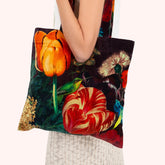 A person carrying a large tote bag with a colorful floral print featuring orange and red tulips, green leaves, and a green hummingbird on a dark background.