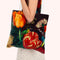 A person carrying a large tote bag with a colorful floral print featuring orange and red tulips, green leaves, and a green hummingbird on a dark background.