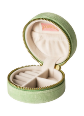 A light green velvet round zipper jewelry box, shown open to reveal a cream-colored interior with multiple compartments and a pink brand label.