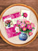 Pop-up card of pink peonies in a blue and white vase, laid on top of the card's envelope, and a matching greeting card. The items are displayed as a flat-lay photo, on top of a ceramic plate on a light wood table.