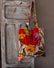 A velvet tote bag with a large orange, red, and pink floral print design hangs on the handle of a grey-washed wooden door.