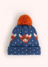 A blue children's knit hat with orange highland cows, white polka dots, and an orange pompom on the top, against a white background.