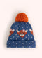 A blue children's knit hat with orange highland cows, white polka dots, and an orange pompom on the top, against a white background.
