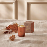 Copper-colored votive candle with decorative box and autumn leaves on a textured surface