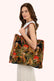 A woman wearing a white sleeveless top and a light-colored knit skirt carries a large quilted tote bag with a detailed woodland print featuring owls, red mushrooms, and green foliage.