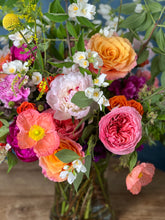 A vibrant, multicolored floral arrangement in a tall glass vase, sat on top of a wooden table. 