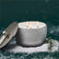 A lit silver candle with white flocking sits with its lid leaning against it, surrounded by fake snow against a forrest green background. 