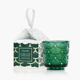 A green tea light candle with a geometric pattern sits next to its accompanying box with an ornament string on it, against a white background.